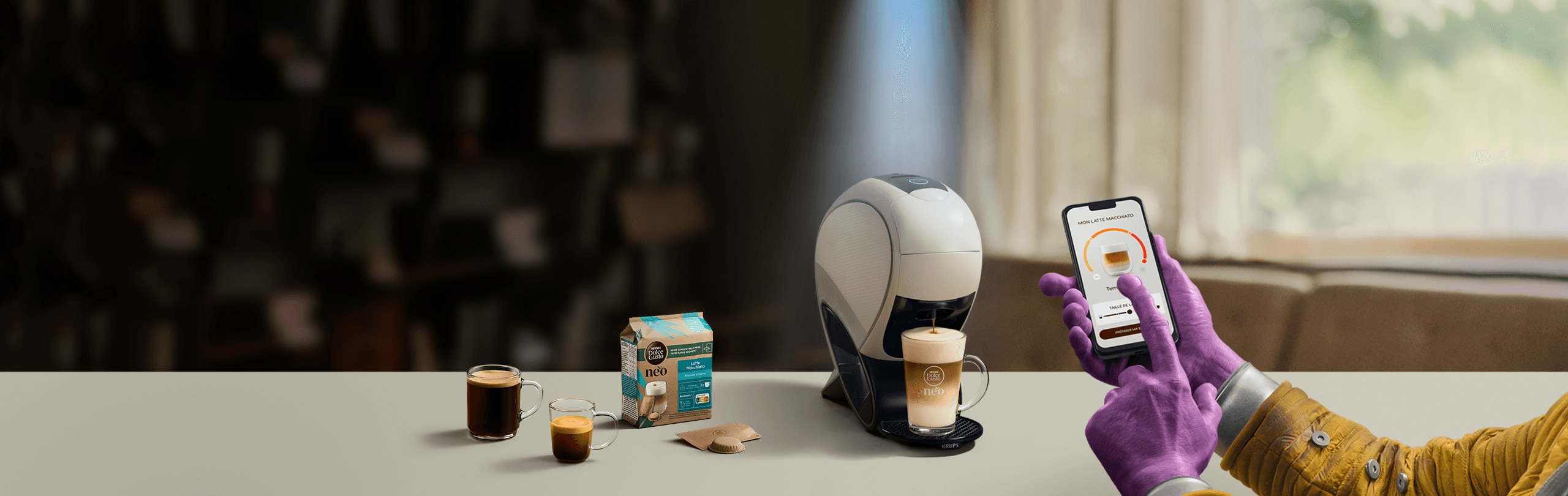 Main d'un extraterrestre utilisant l'application NESCAFE Dolce Gusto pour personnaliser son café. En arrière-plan, la machine NEO, des boîtes de dosettes et des boissons.