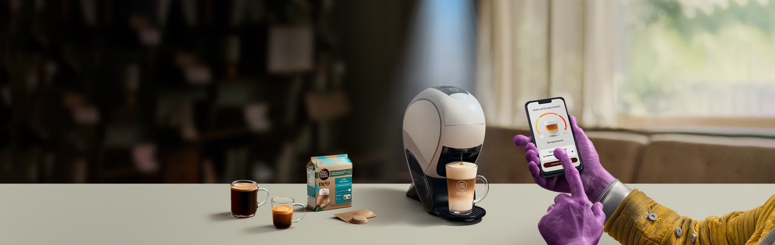 Eine Alien-Hand nutzt die NESCAFÉ® Dolce Gusto® App, um einen Kaffee zu personalisieren. NEO Latte Kaffeemaschine, Kaffee-Pack und Getränke.