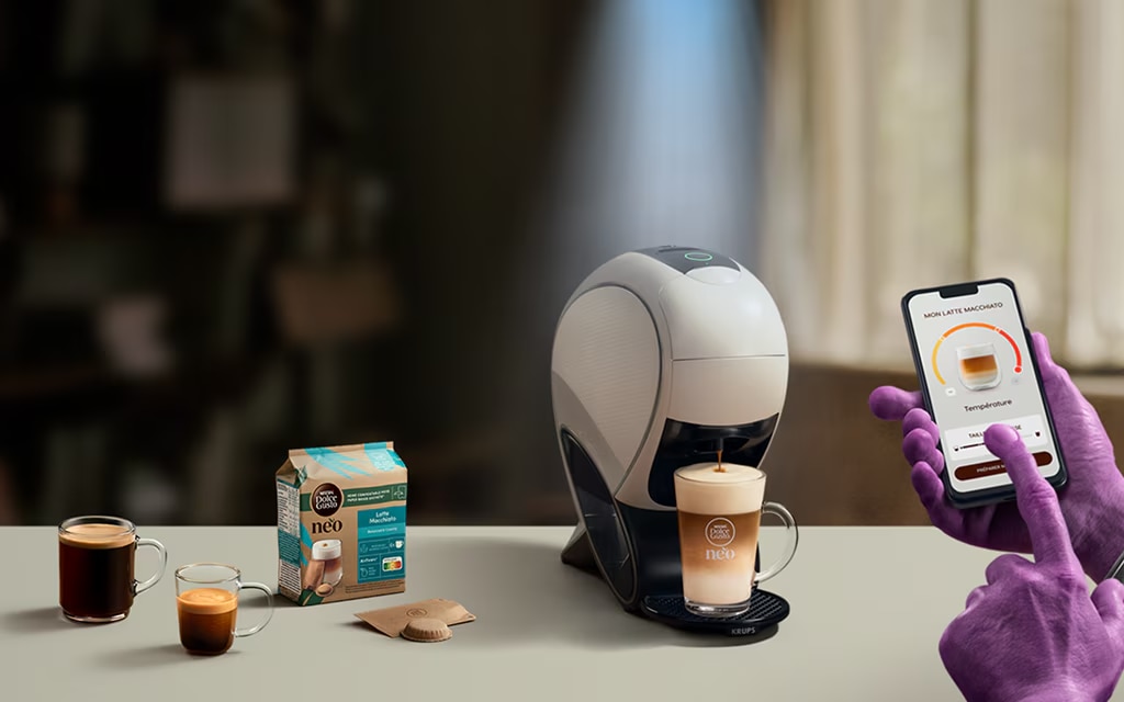 Eine Alien-Hand nutzt die NESCAFÉ® Dolce Gusto® App, um einen Kaffee zu personalisieren. NEO Latte Kaffeemaschine, Kaffee-Pack und Getränke.