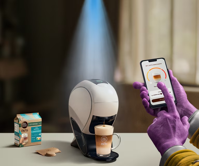 Eine Alien-Hand nutzt die NESCAFÉ® Dolce Gusto® App, um einen Kaffee zu personalisieren. NEO Latte Kaffeemaschine, Kaffee-Pack und Getränke.
