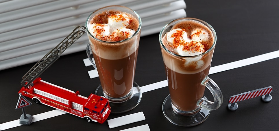 Zwei Tassen CHOCOCINO® mit Marshmallows und Chili oben drauf, daneben ein Spielzeug-Feuerwehrauto