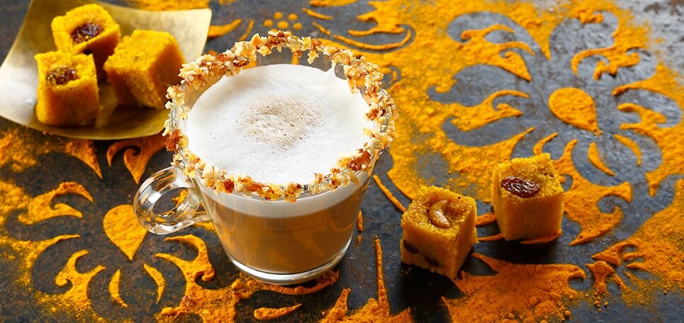 Ein Glas Chai Tea Latte, am Rand drappiert mit einer Masse aus Karamell, Trauben und Nüssen sowie Cashew-Trauben-Würfeln
